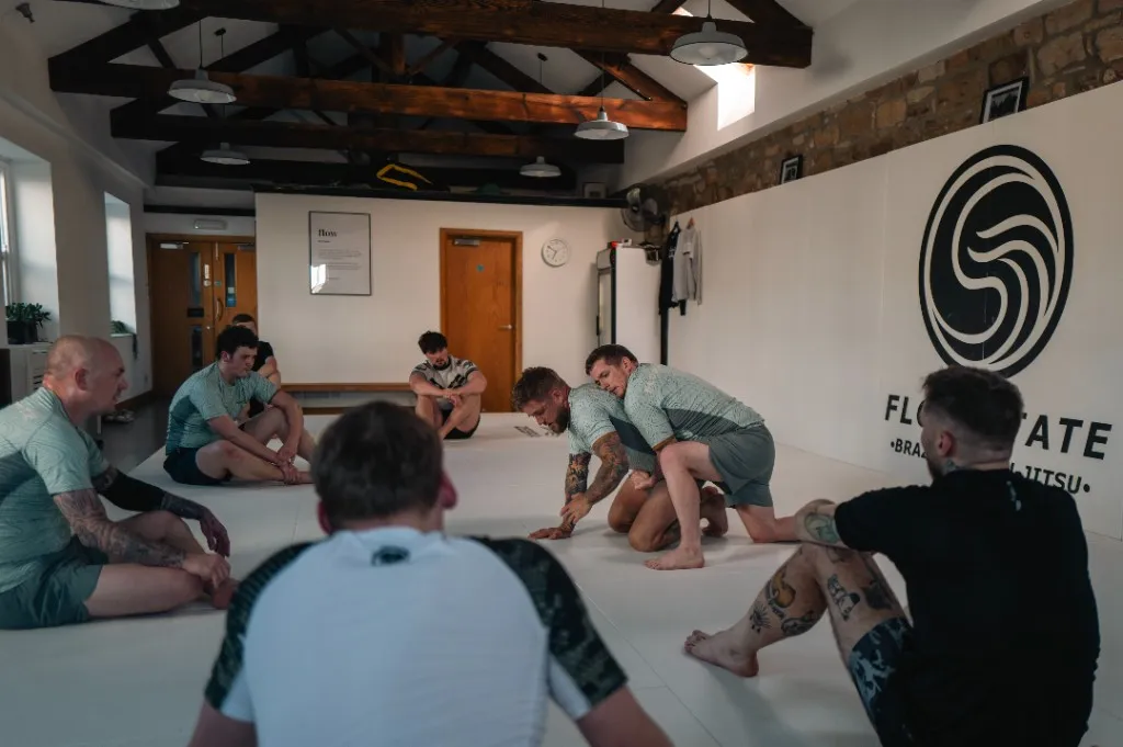 A group of students watching a technique demonstration during a Brazilian jiu-jitsu class at Flow State BJJ.